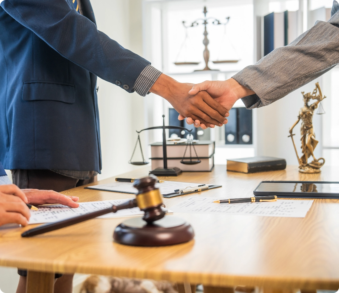 A lawyer and client shake hands over a table next to a gavel after securing a legal deal.